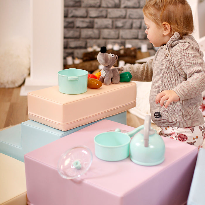 A young girl developing her coordination and gross motor skills while playing with an IGLU Soft Play Soft Play Foam Block Set - Corner Climber toy on top of a stack of boxes.